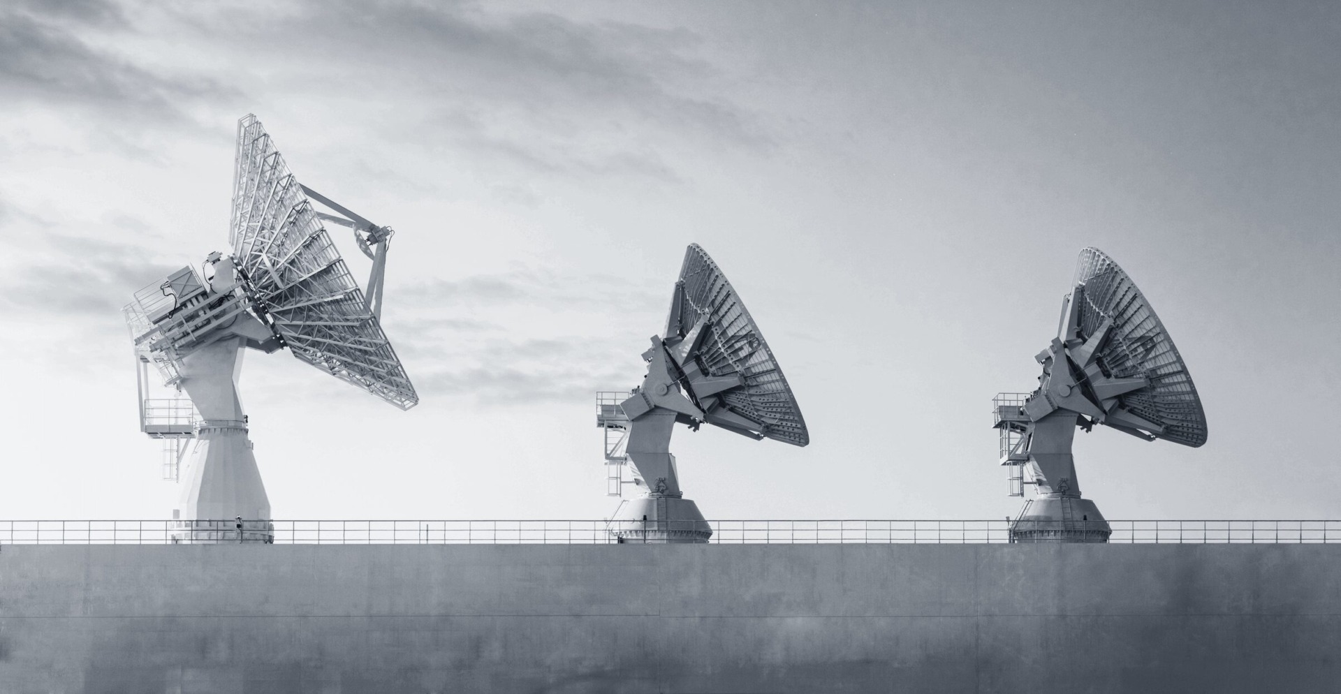 Three large, white satellite dishes against a cloudy sky, representing advanced technology for compliance monitoring.